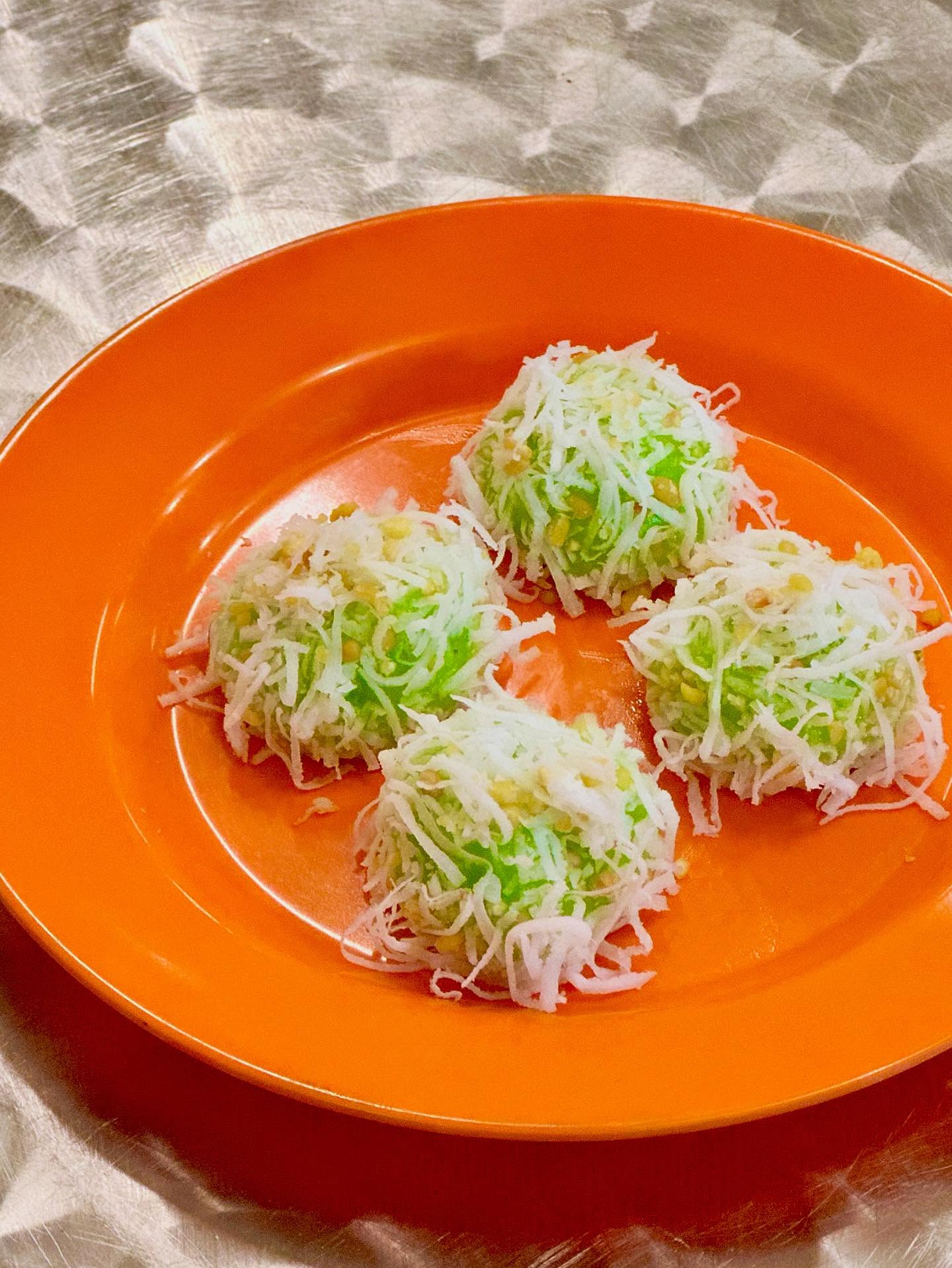 Four coconut-topped green Thai desserts on an orange plate