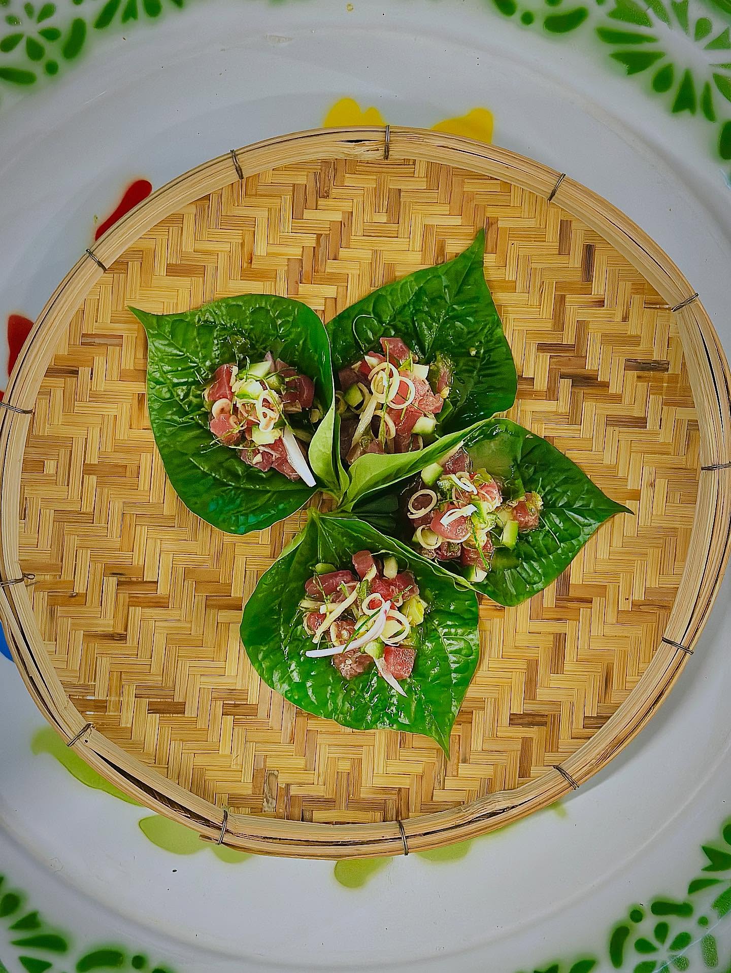 Betel leaf bites topped with fresh herbs, served on a woven bamboo tray