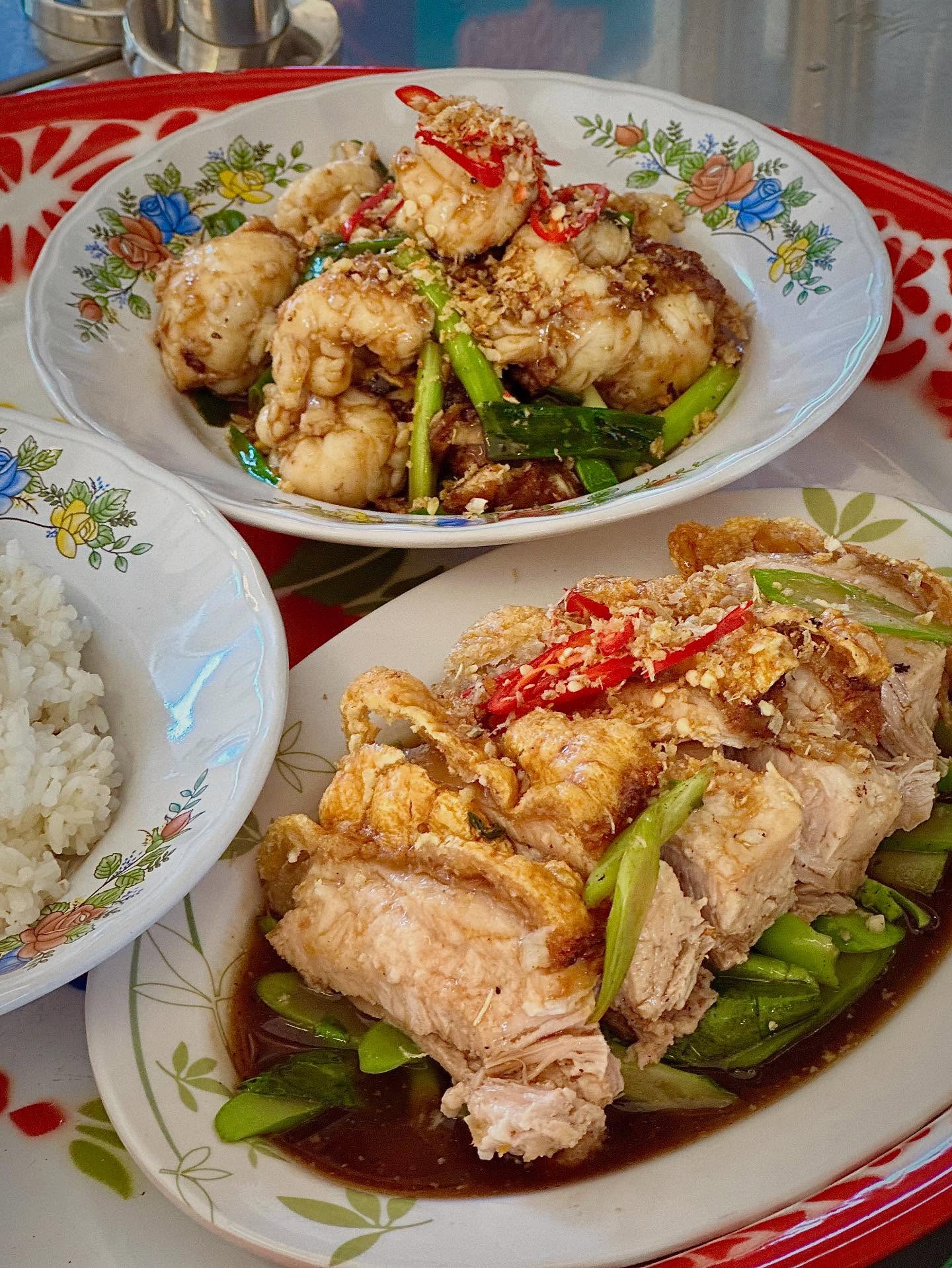 Two Thai dishes on floral plates with steamed rice, topped with fresh chilli